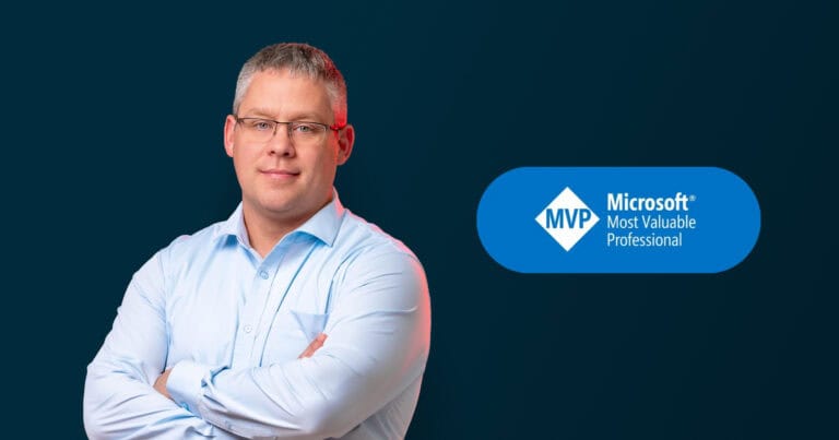 The image features a man with short gray hair and glasses, wearing a light blue button-up shirt. He is standing with his arms crossed, exuding a professional and confident demeanor. The background is a solid dark blue, creating a stark contrast with his light-colored shirt. To the right of the man, there is a blue oval-shaped badge with the text "MVP Microsoft Most Valuable Professional" inside it. The overall composition highlights the man's professional achievement and recognition by Microsoft.