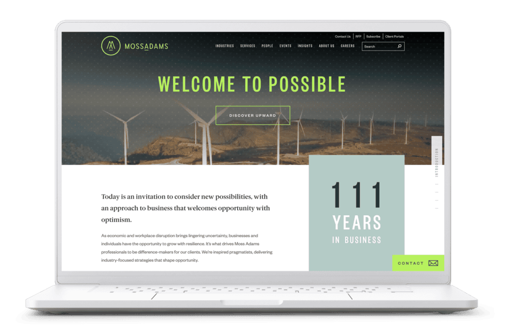 A laptop displaying the Moss Adams website. The screen shows the Moss Adams logo and navigation bar at the top, with a hero image of wind turbines in the background and the prominent text "WELCOME TO POSSIBLE." Below that, there is a call-to-action button labeled "DISCOVER UPWARD." On the right side, there's a highlight section that reads "111 YEARS IN BUSINESS" in large text. The overall theme is clean and professional, using green, gray, and white color tones that emphasize the brand's forward-thinking and established presence.