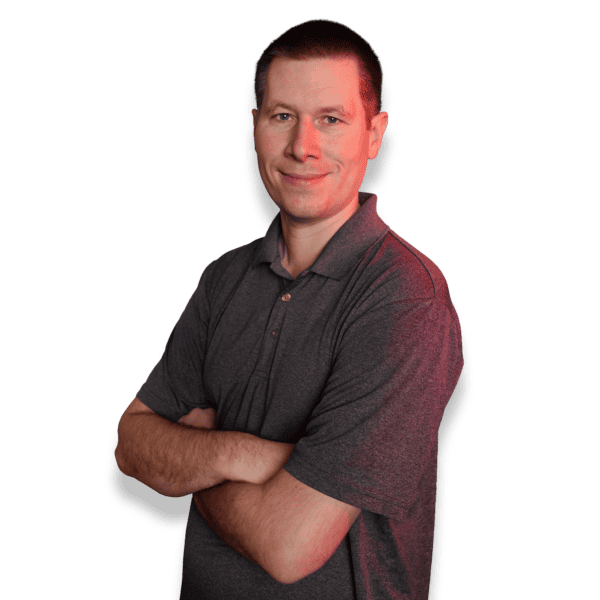 Person with short dark hair, wearing a gray polo shirt, standing confidently with arms crossed against a black background, with a subtle red lighting effect on one side.